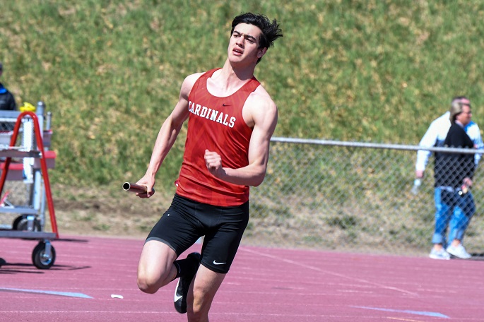 A young man sprinting on a track, passing a baton to his teammate during a relay race.