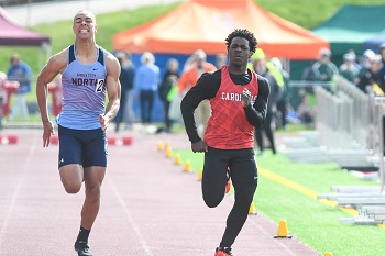 Two men sprinting on a track with spectators cheering in the background.