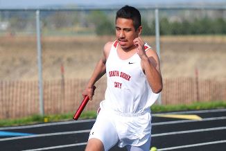 A young man sprinting on a track with a bat in hand.