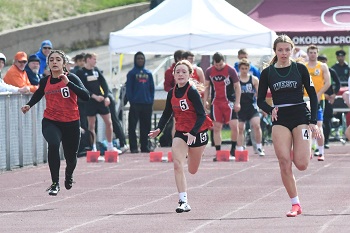 Girls sprinting in a track race, with enthusiastic spectators cheering from the sidelines.