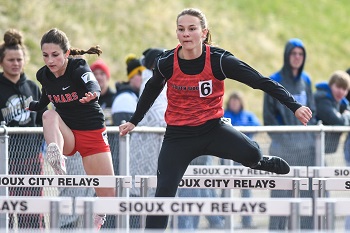 Two women sprint over hurdles in a competitive race, showcasing athleticism and determination on the track.
