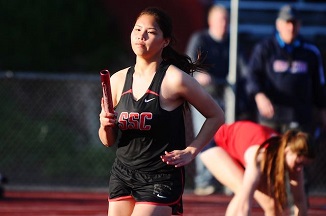 Young girl sprinting on track, passing baton in relay race.