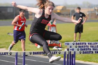 Young female athlete leaping over hurdle during track race.