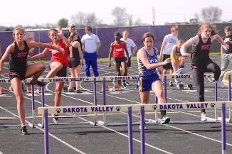 Girls running over hurdles on a track during a race.