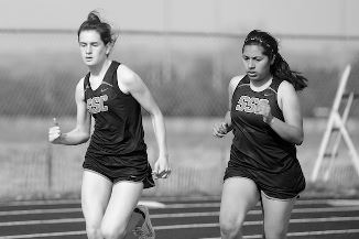 Two girls running on a track in black and white, showcasing determination and teamwork.