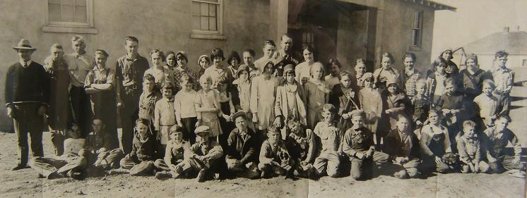 An old photograph depicting a group of children and adults gathered together, showcasing their joyful expressions and attire.