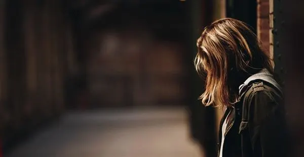 A woman stands in a hallway, facing away from the camera, highlighting the corridor's length and her silhouette.