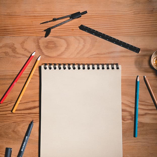 A neatly organized workspace featuring a notepad, pencils, and pens.