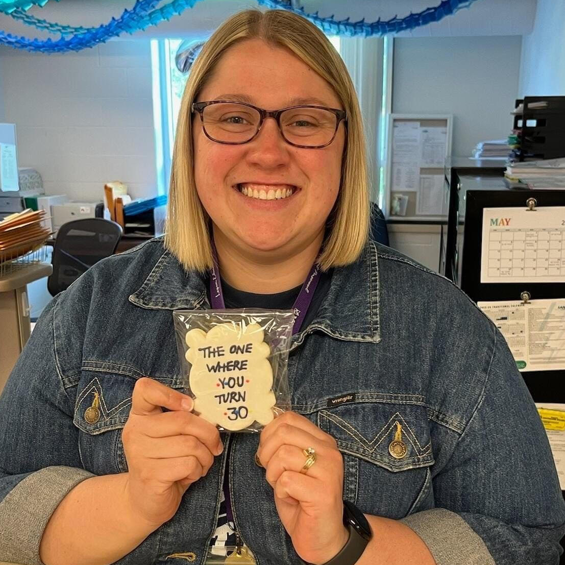 Picture of a blonde female with glasses holding a card that says The One Where You Turn 30