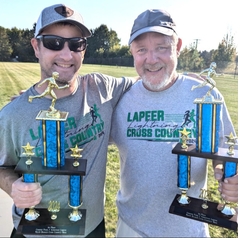 Two high school male cross country coaches with trophies