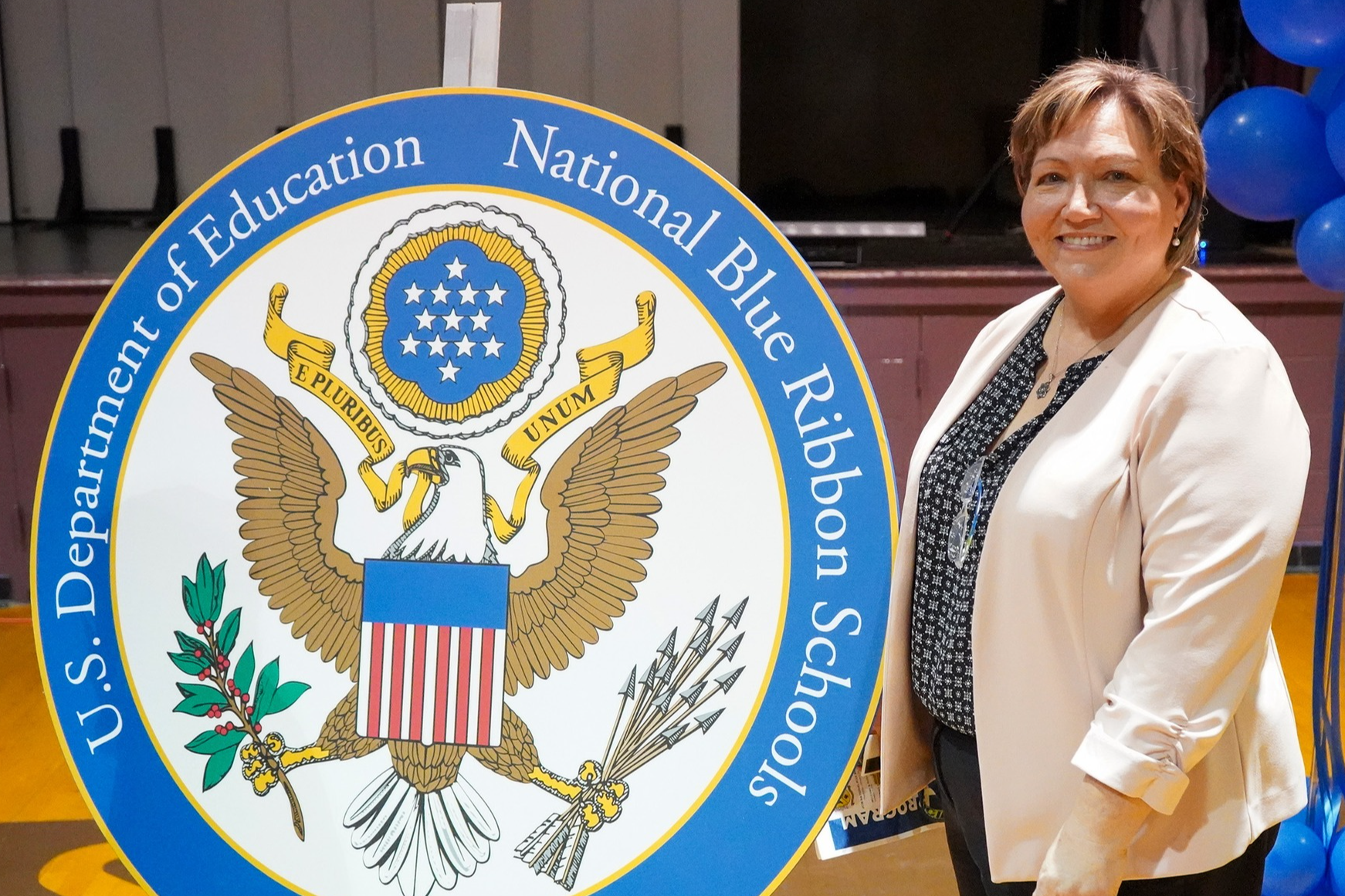 Principal Lightsey stands next to the National Blue Ribbon Schools seal from the U.S. Department of Education