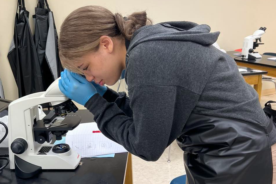 High school student looking into a microscope. 