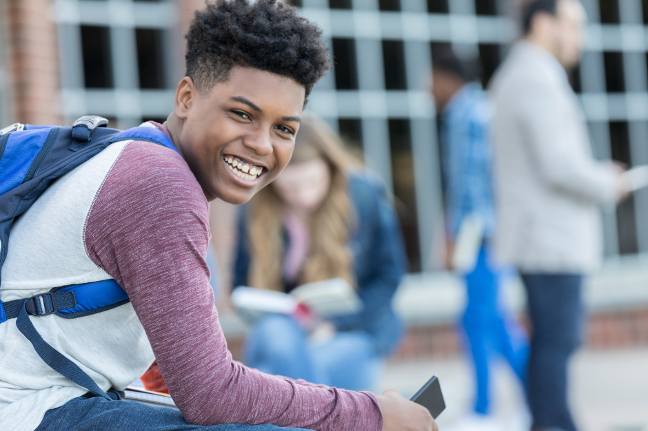 Male student standing with a backpack on one shoulder and holding books. 