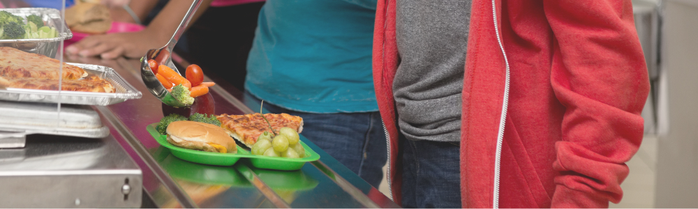 Children putting fruits and vegetables on their lunch tray. 