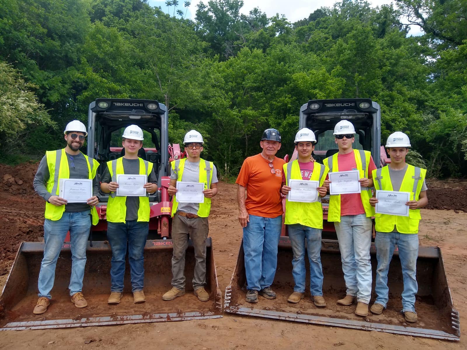 Students are wearing safety vests and hard hats. They are displaying the skid steer certification they earned. 