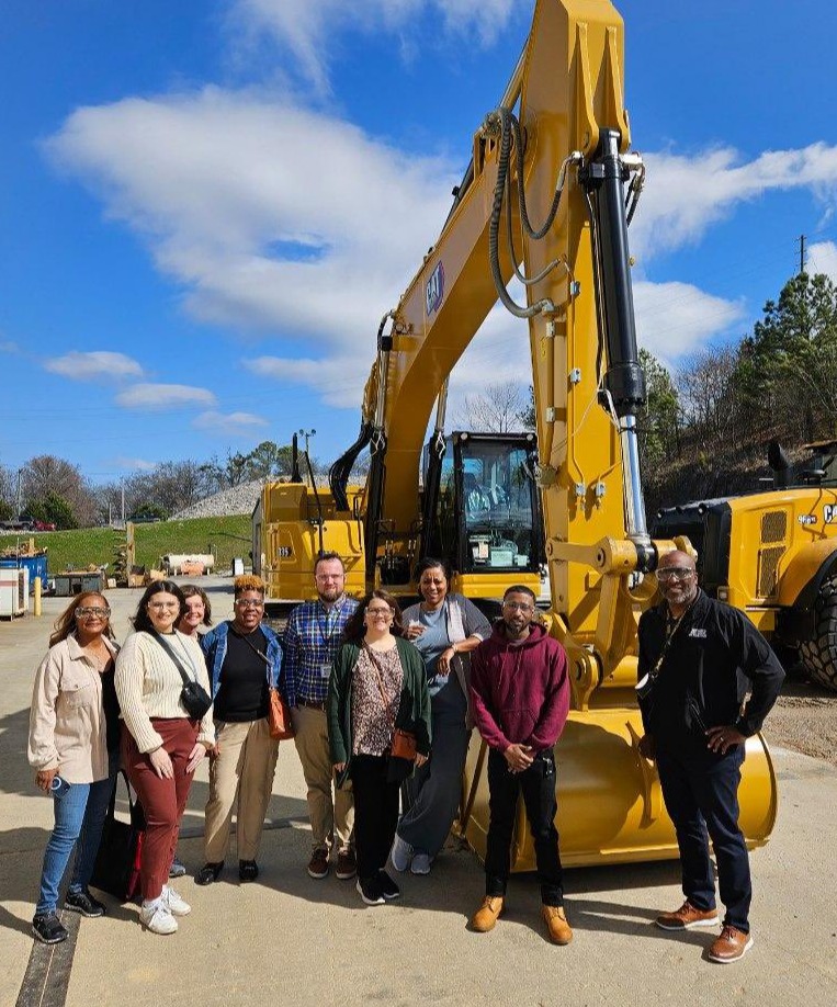 Students stand in front of a large piece of construction equipment. 