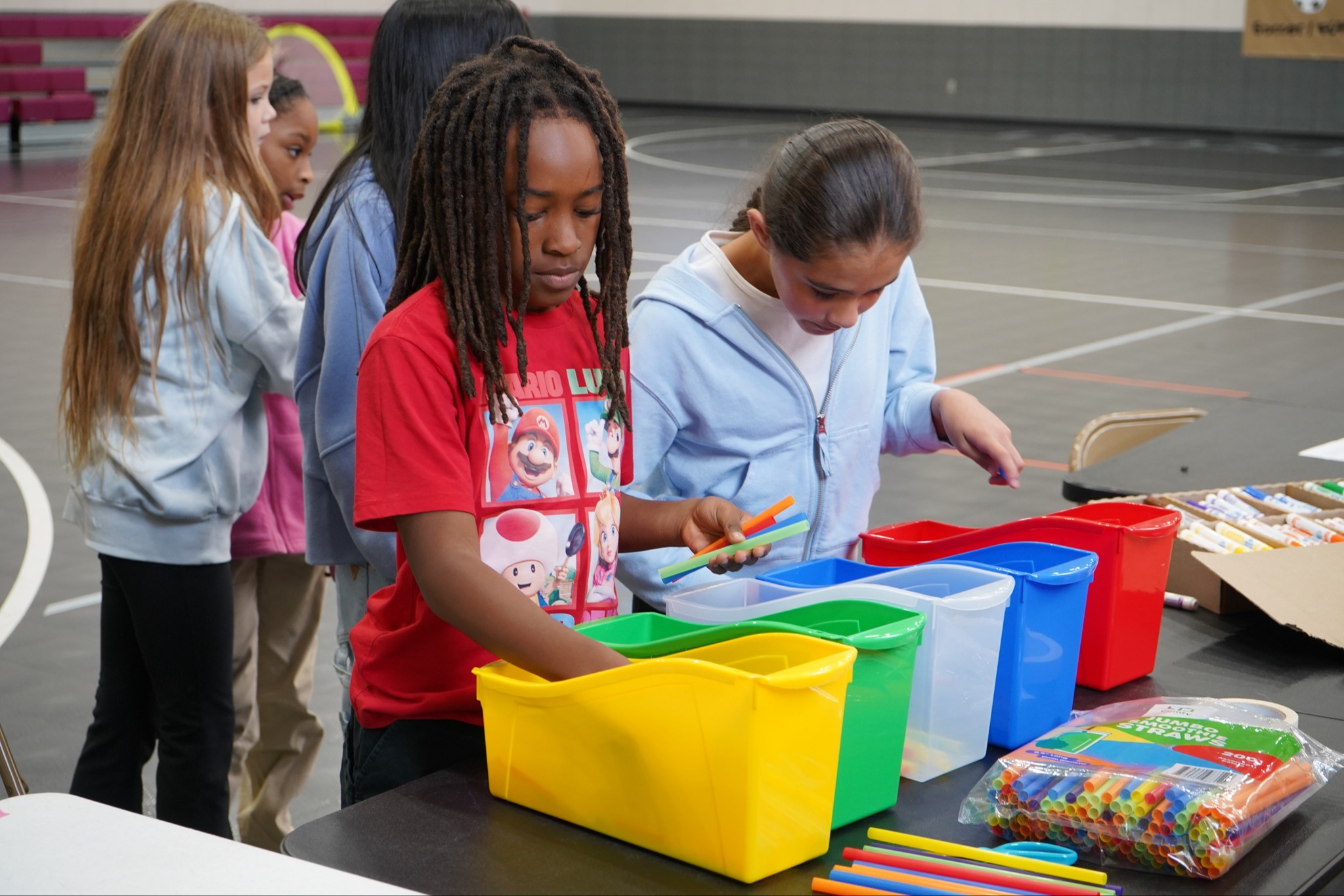 Students working on a project. They are reaching into colorful storage boxes and have colorful straws in their hands.