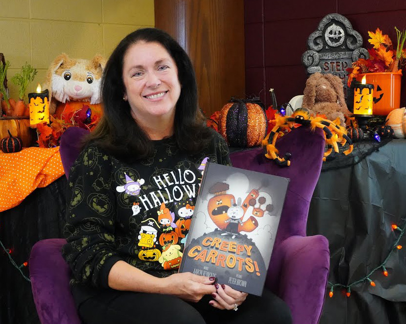 Dr. Leslie Richards holds up the book Creepy Carrots! She is sitting in front of a spooky background. 