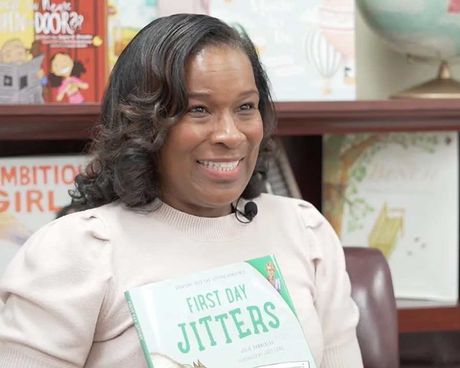 Dr. Angela Watkins is smiling and holding the book titled First Day Jitters