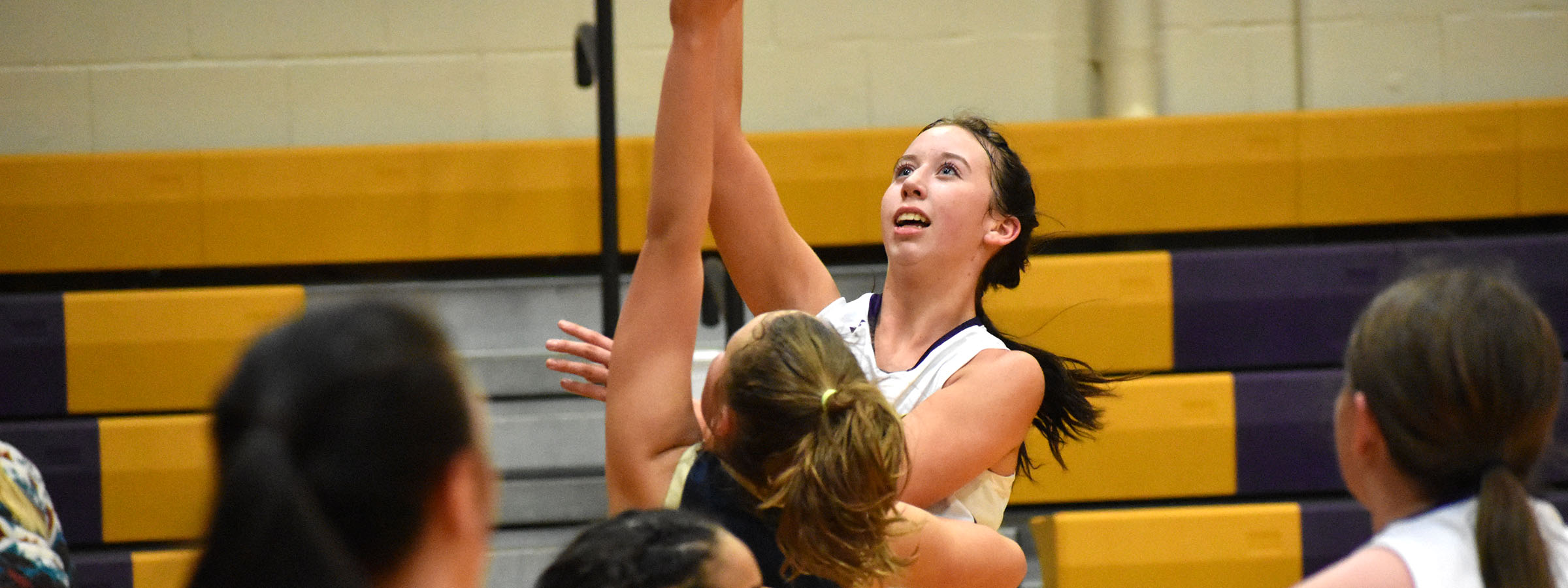 A girl in a purple and white uniform reaching for the ball on the field.