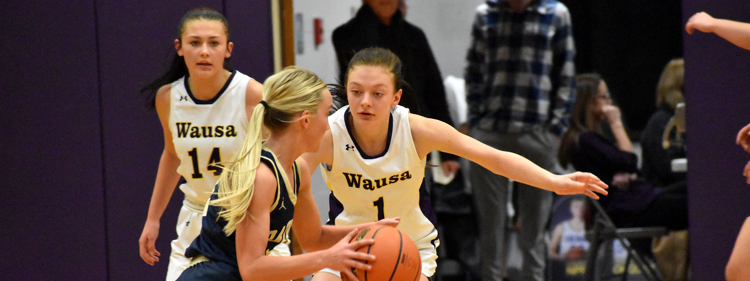 Two girls in basketball uniforms compete fiercely during a game, showcasing their skills and teamwork on the court.