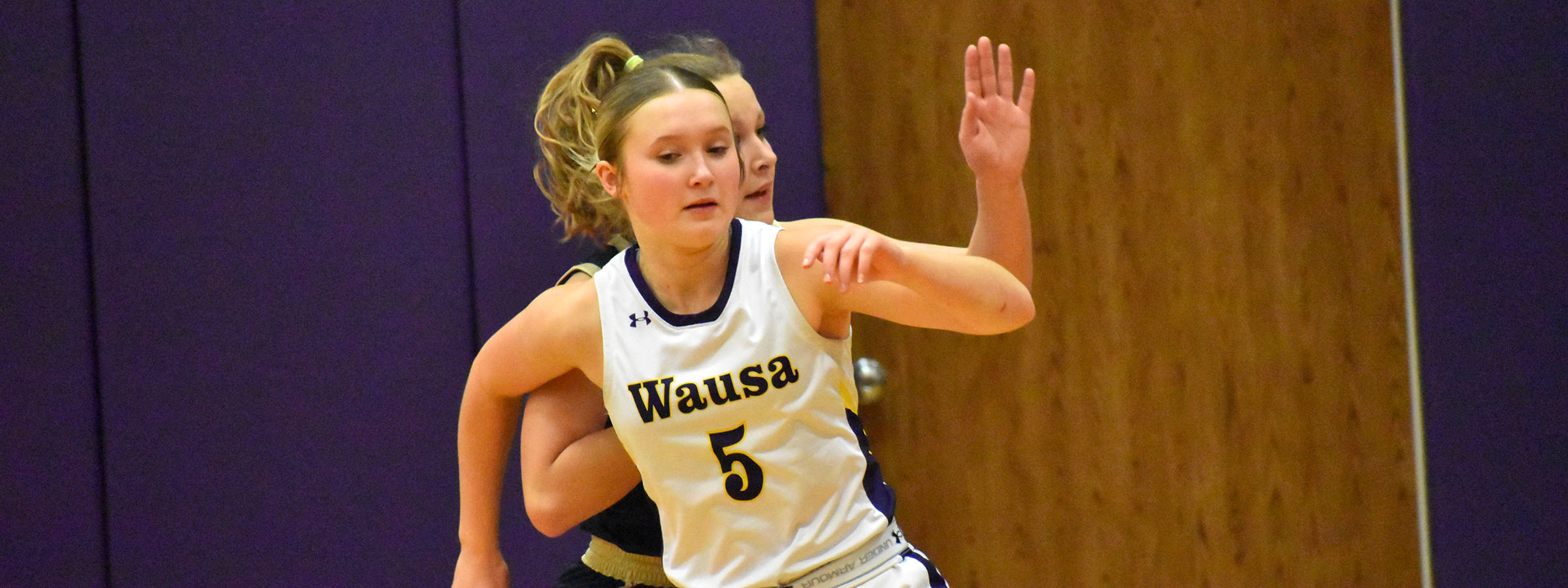 A girl in a white uniform holding a basketball.