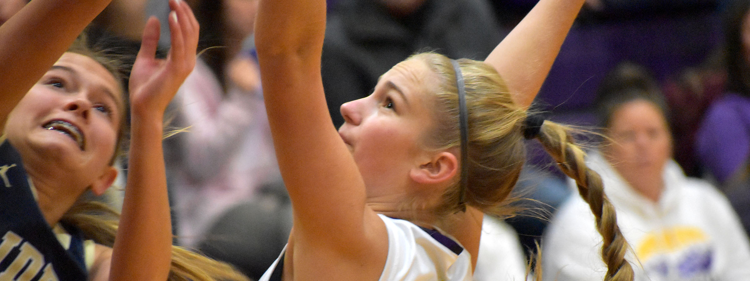 Two girls playing basketball, one reaching for the ball.