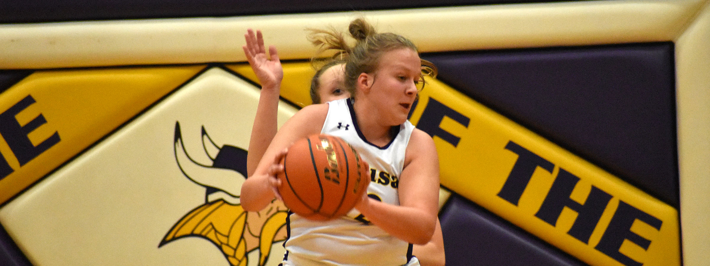 A young female athlete in a white uniform with a basketball.