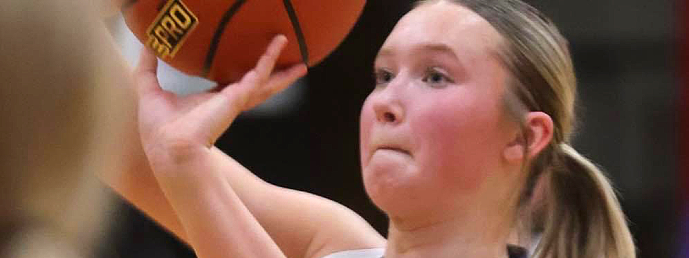 A girl in a white shirt and black shorts holding a basketball.