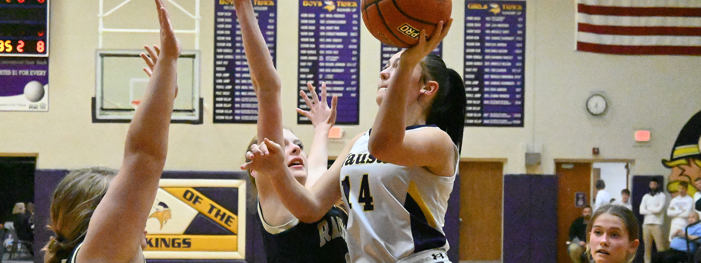 A girl in a white uniform attempting to block a shot during a basketball game.