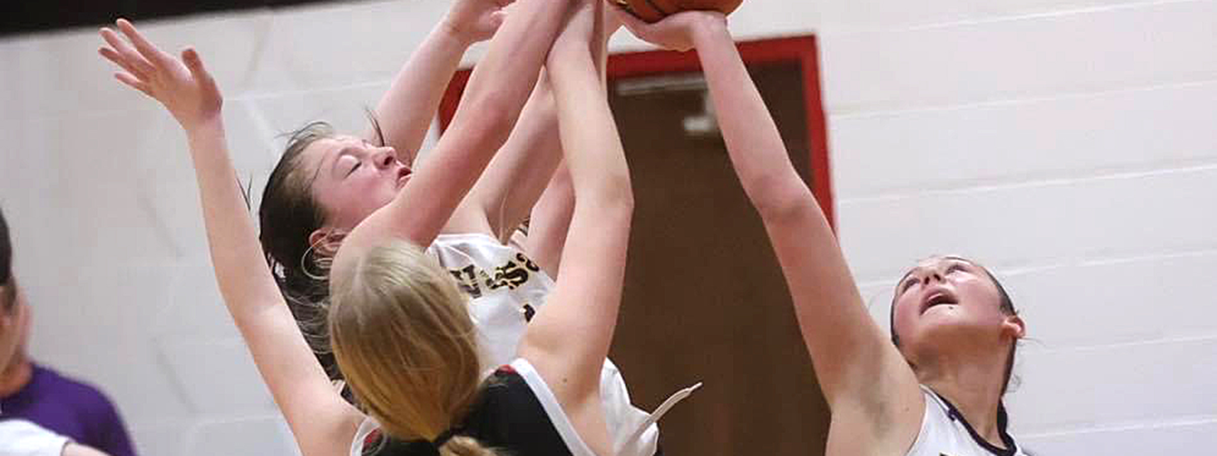  Three girls in black and white uniforms dribble a basketball on the court, showcasing teamwork and athleticism.