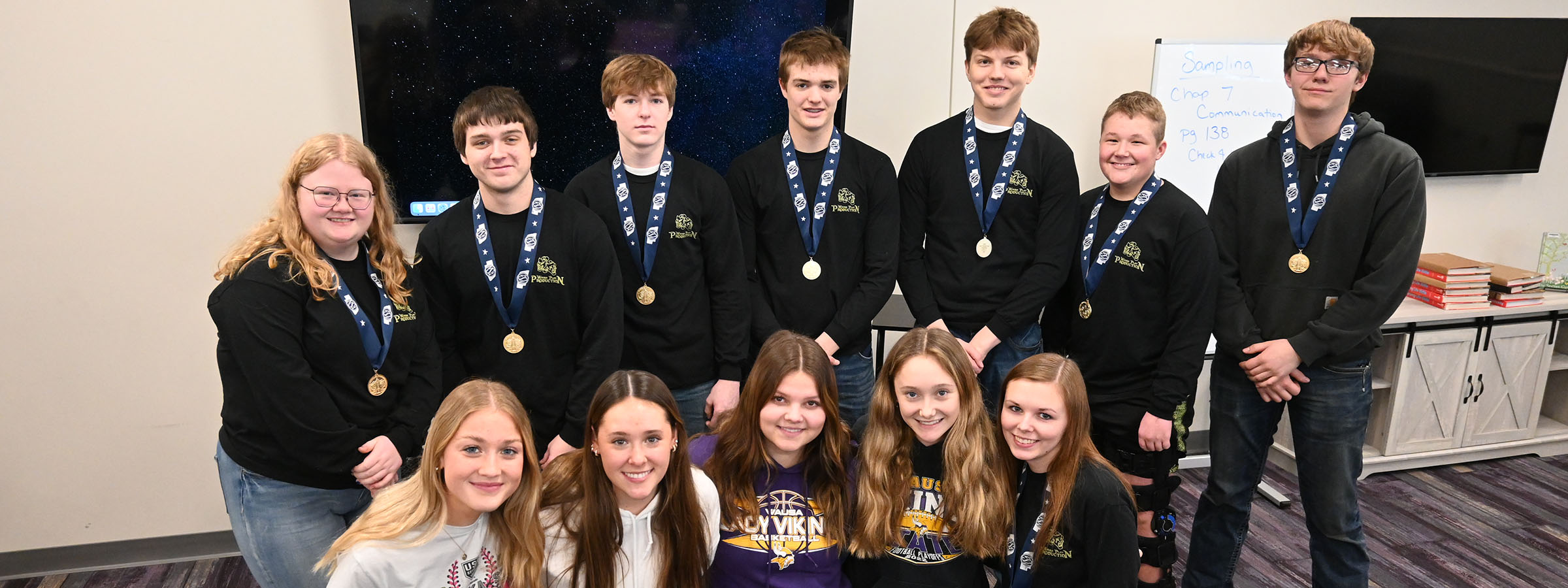 A group of students proudly displaying their medals while posing for a celebratory photo together.