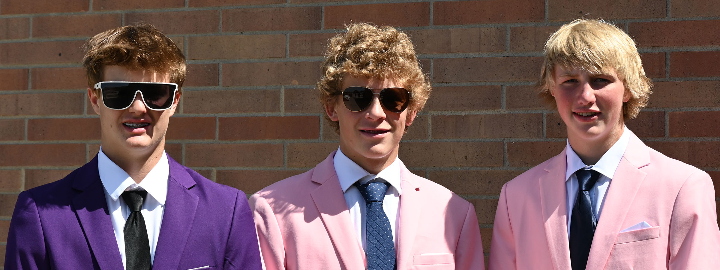 Three young men in suits and sunglasses posing confidently.