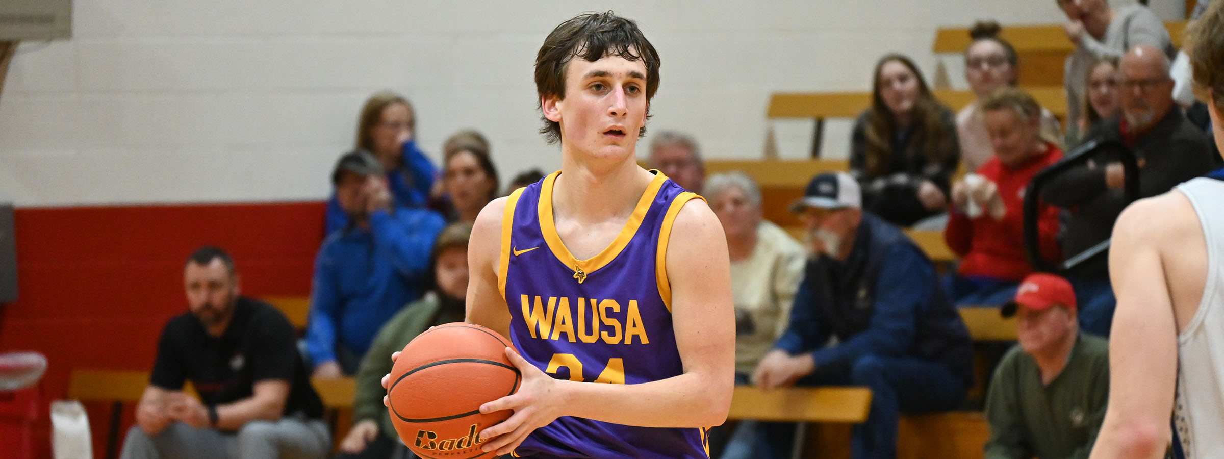 A young man in a purple and gold uniform holding a basketball.