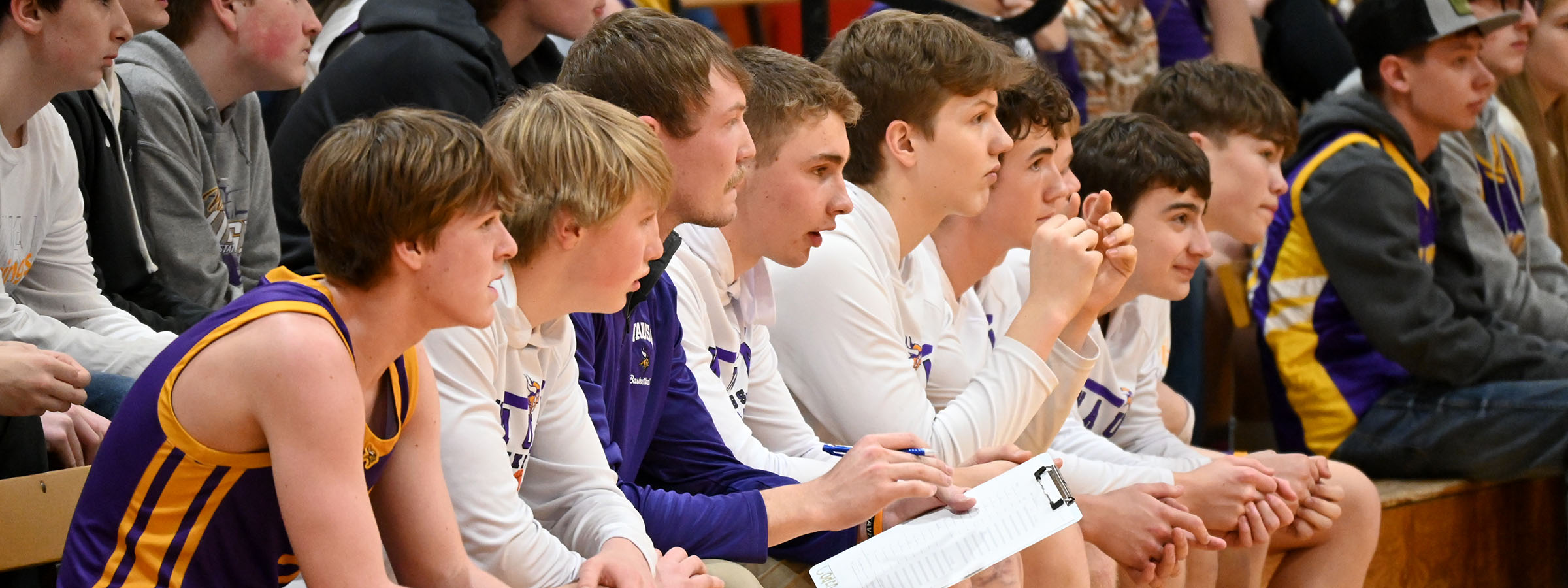 A boys basketball team sits on the bench, focused and ready, as they watch the game unfold on the court.