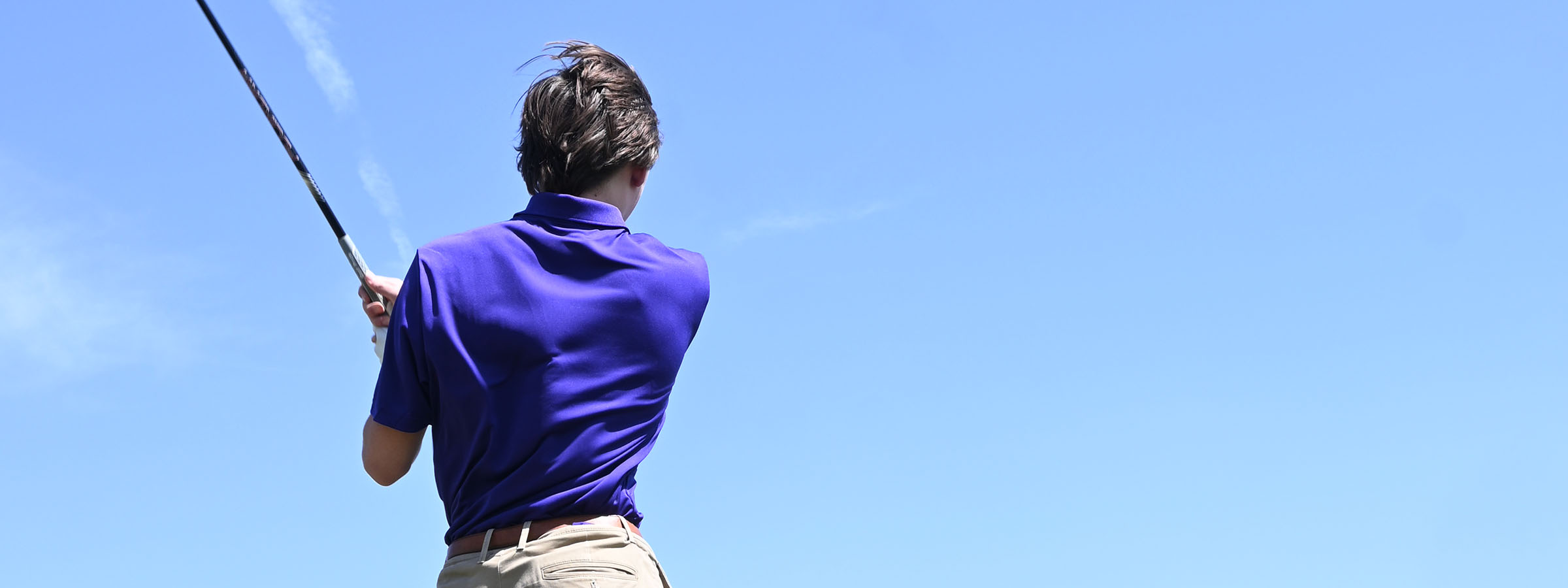 Man in purple shirt swinging golf club on green grass.