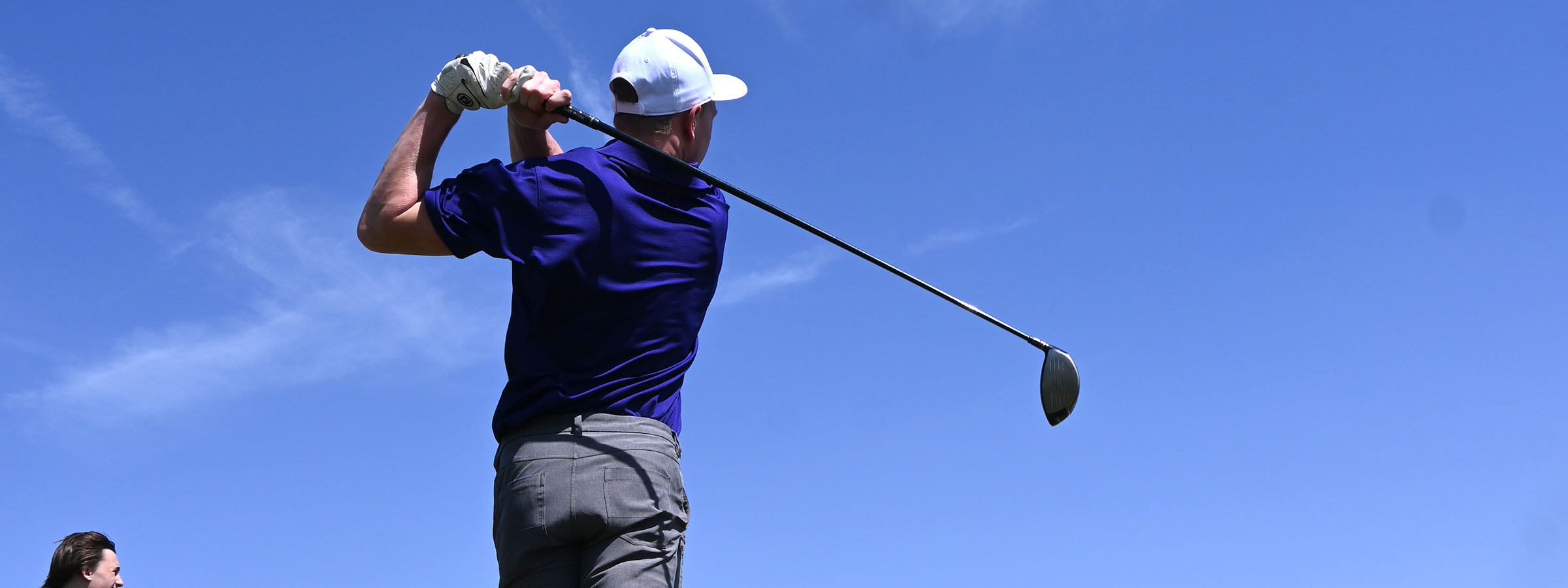 Man swinging golf club under clear blue sky.