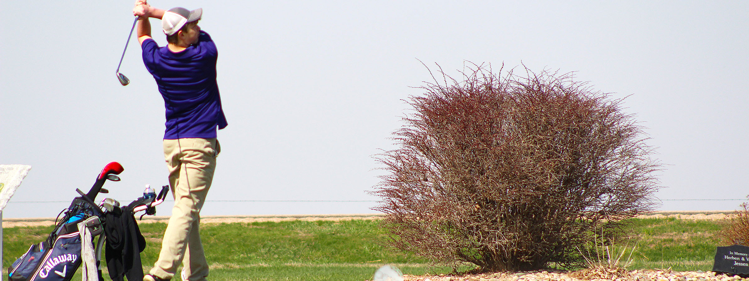 Golfer swinging club on green grass.