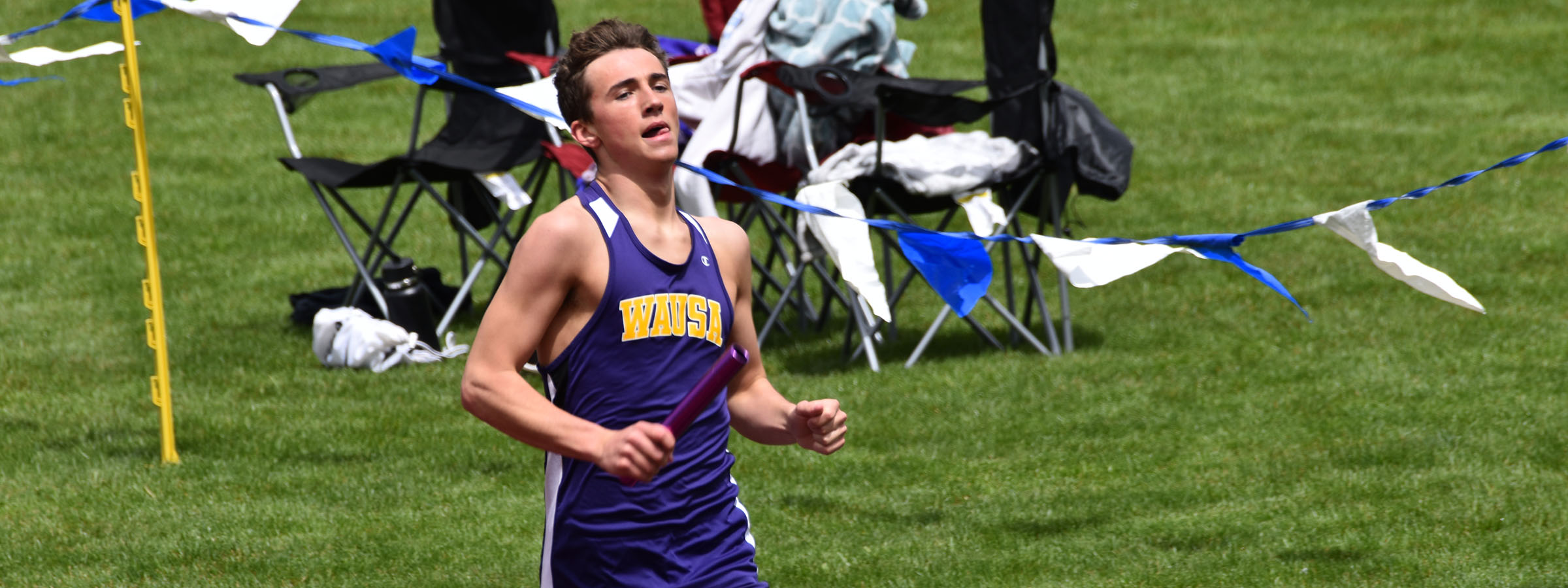 A male athlete in a purple uniform running on the track.