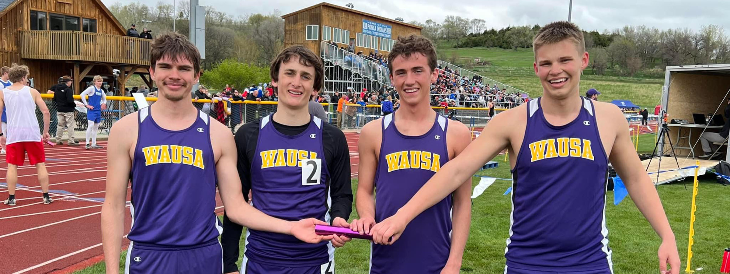  Four young men wearing purple and white track uniforms stand together, smiling and ready for their next race.