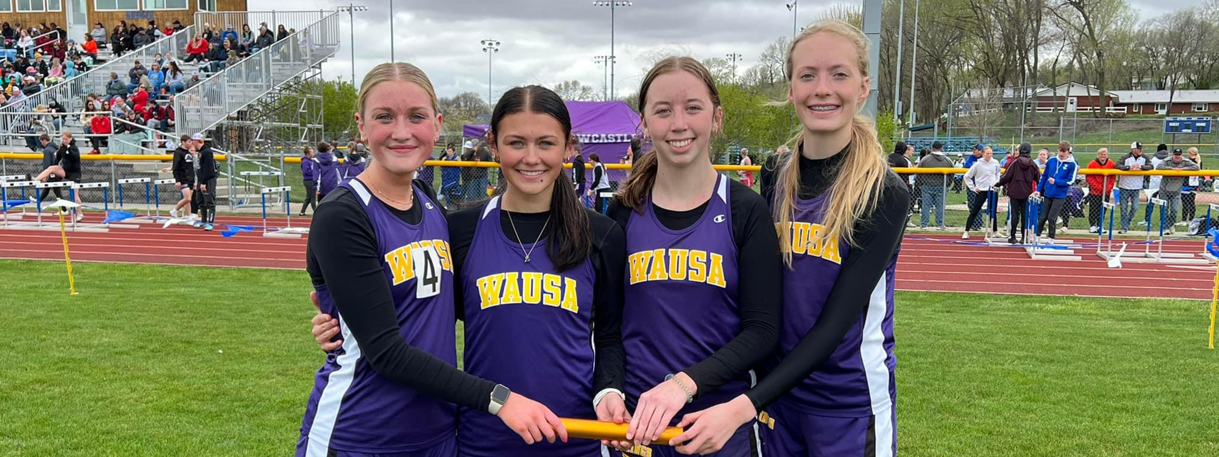 Four girls in purple uniforms smiling and holding a ribbon.