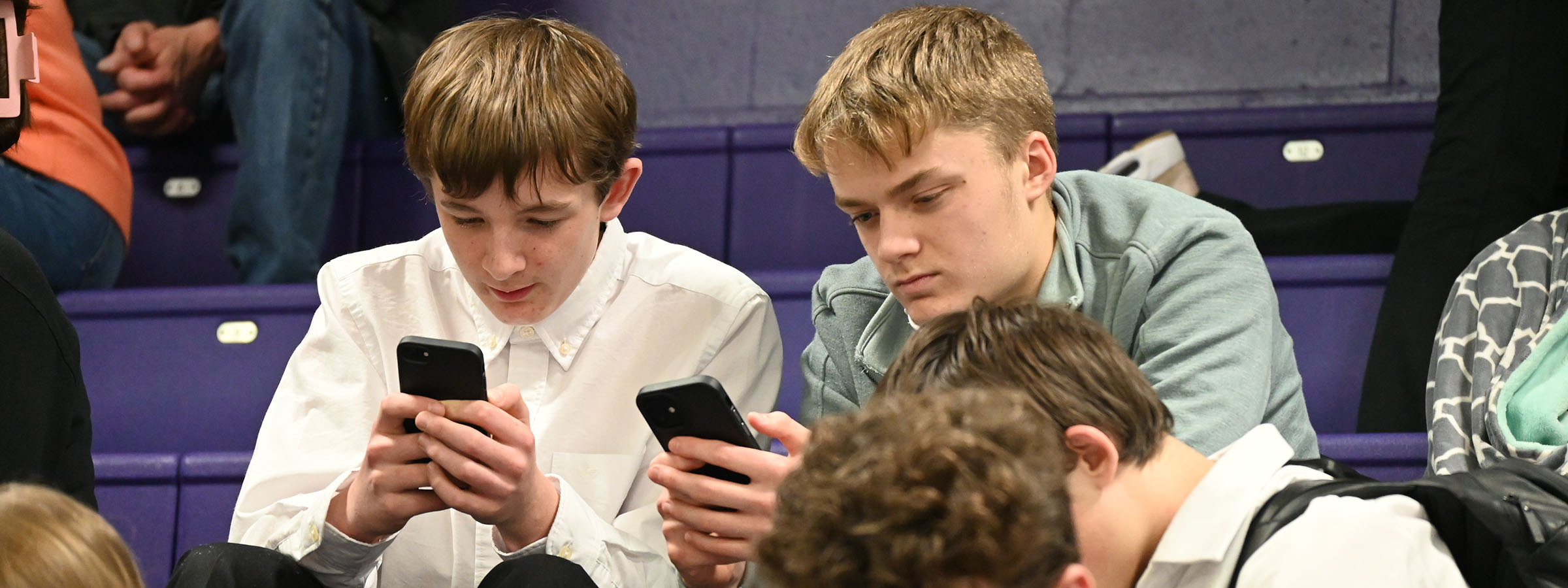 Two boys sitting on bleachers, engrossed in their phones.