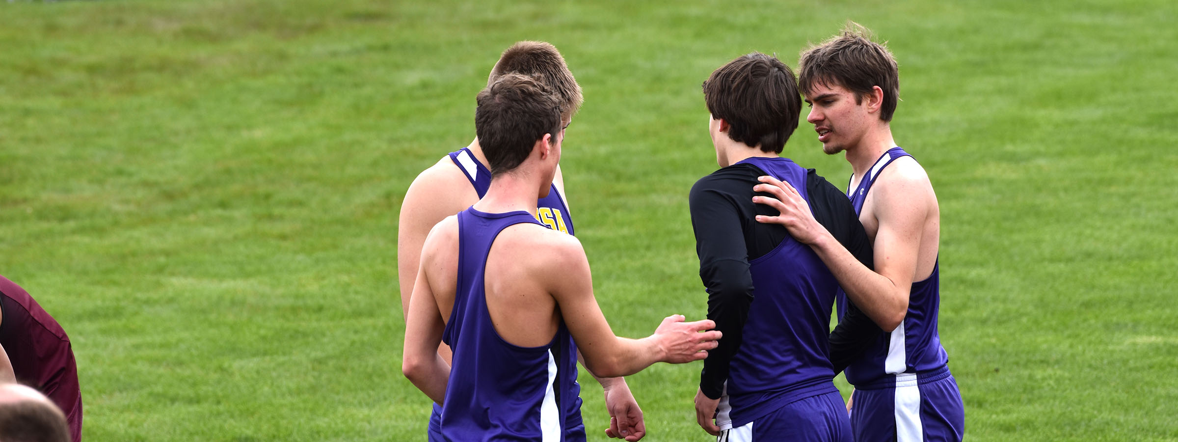 A group of boys huddled together on a grassy field, engaged in a moment of camaraderie and teamwork.