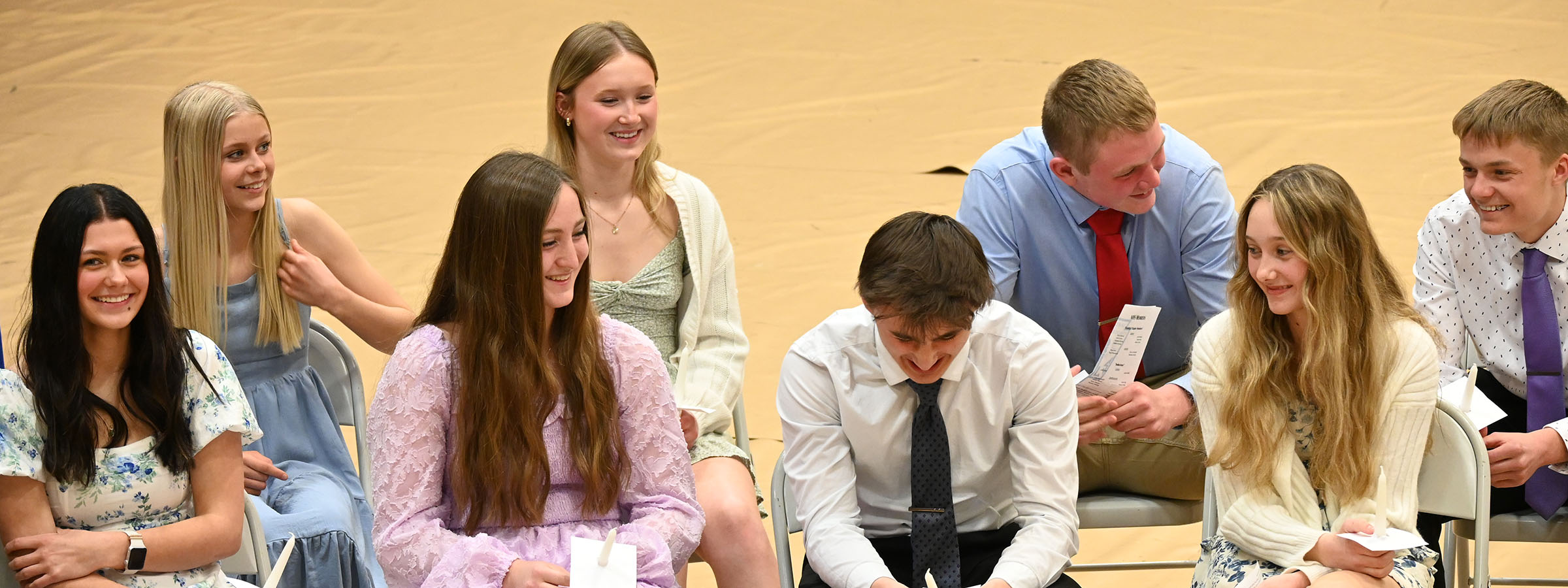 A diverse group of young people sitting on chairs, engaged in conversation and smiling.