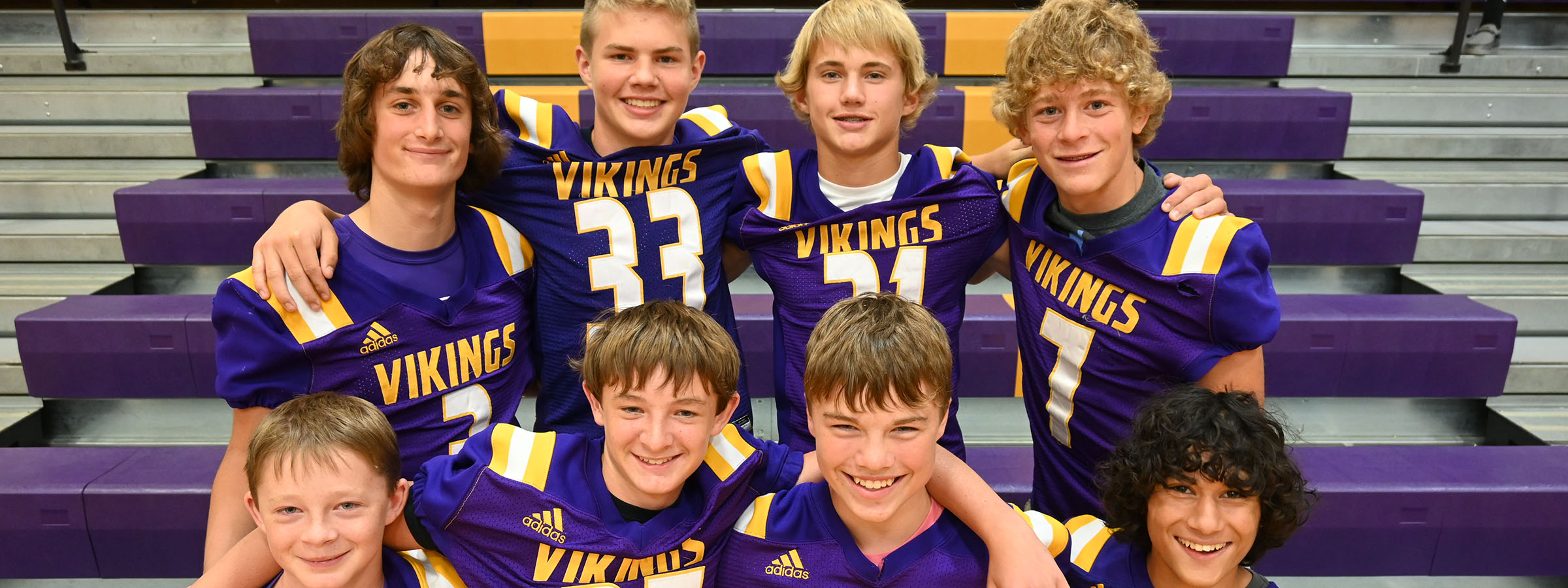 A group of young boys in purple and gold uniforms standing together on a sports field.