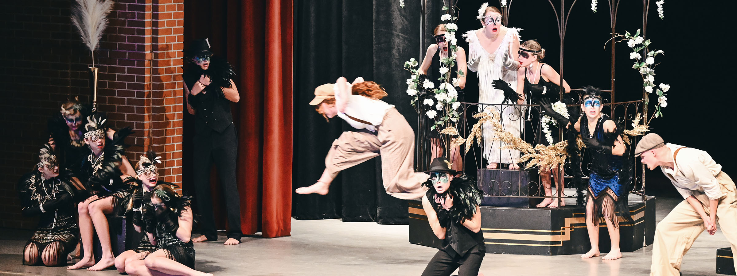 A group of people performing on stage with theatrical masks.