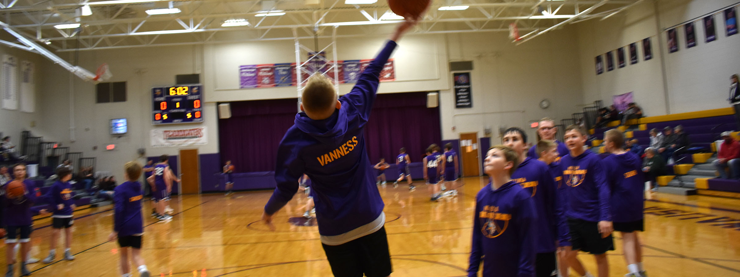 A boy in a purple shirt leaping to catch a basketball.