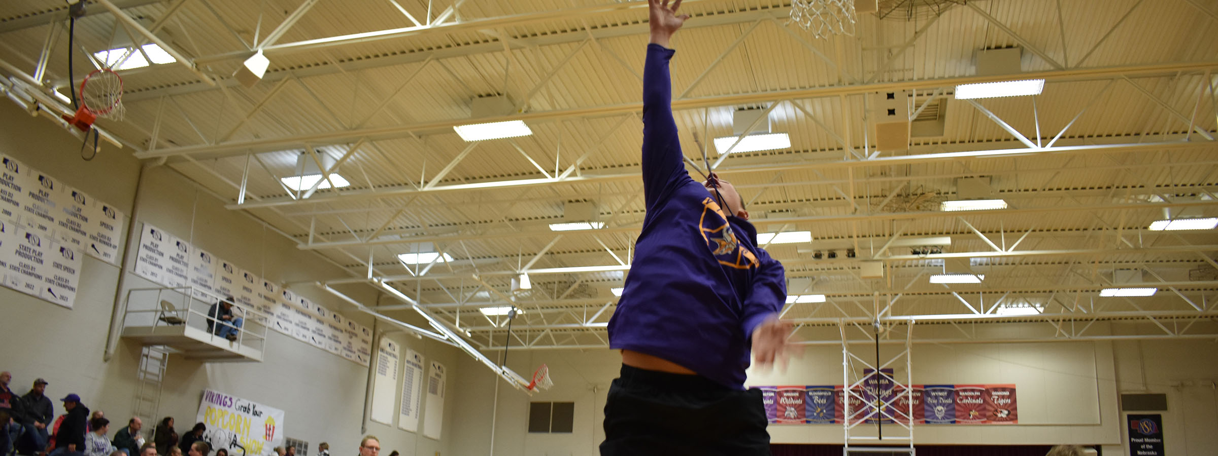 A man in a purple shirt jumps to shoot a basketball 