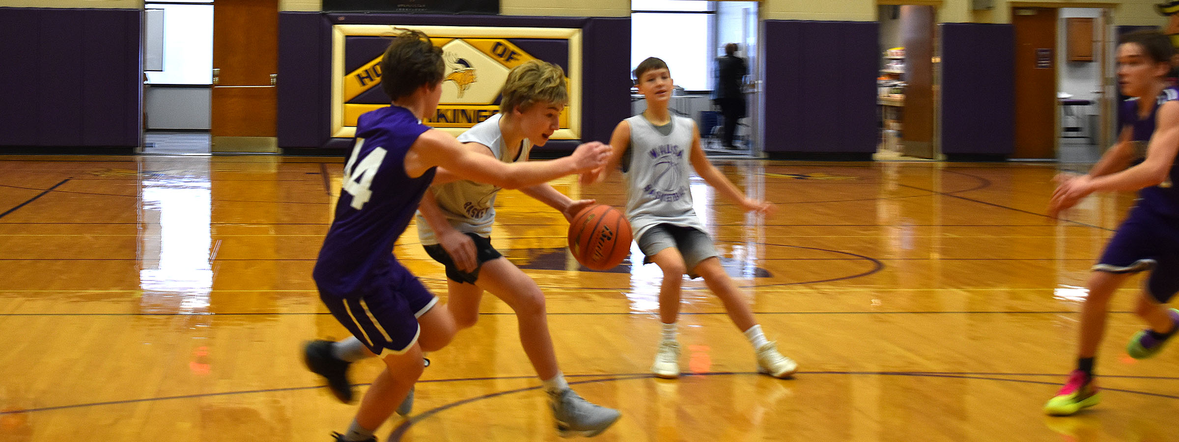 Young basketball players practice in a gym, dribbling and shooting hoops.