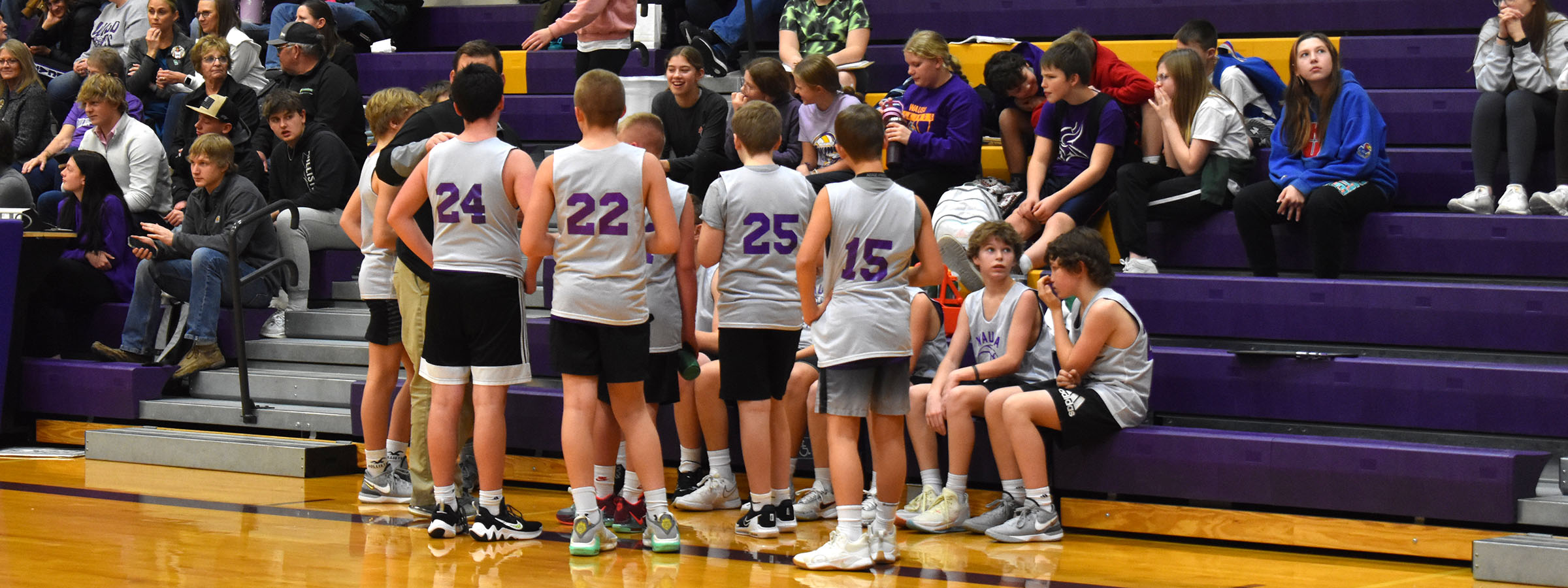 Several boys sitting on gym bleachers, chatting and watching a game.